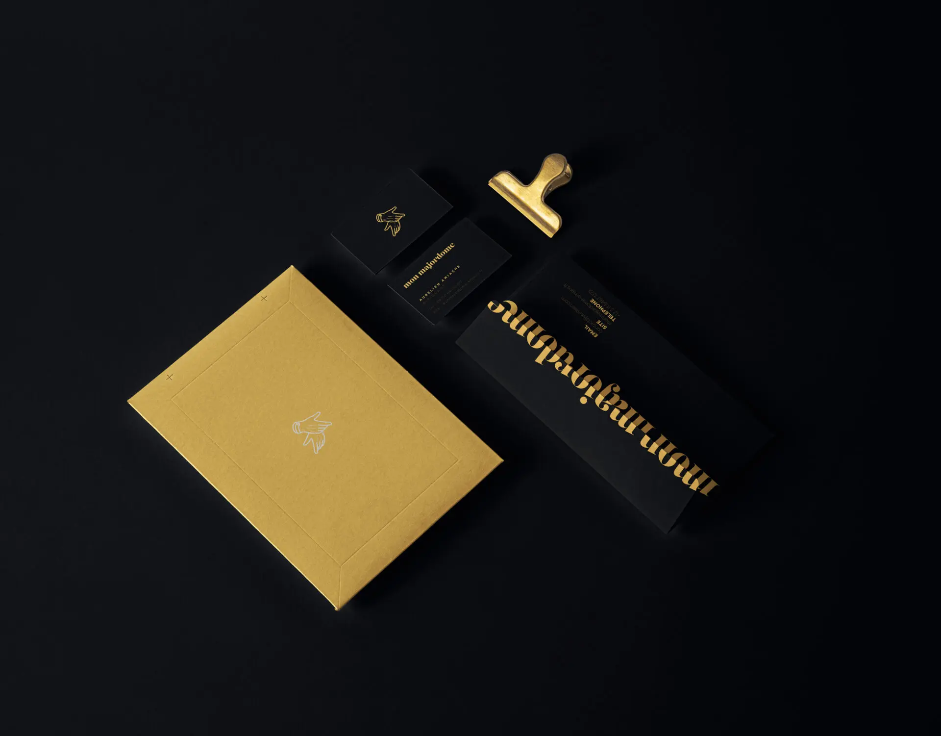 Papeterie Mon Majordome sur fond noir, avec une pochette dorée, des cartes noires et une pince en métal doré.