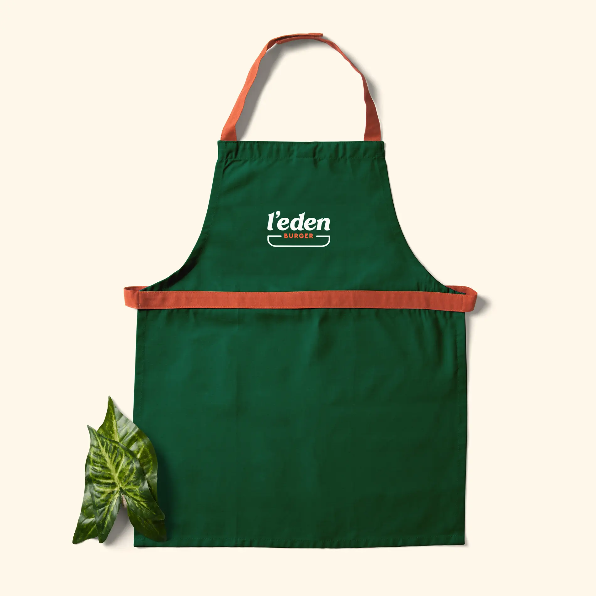 Tablier vert portant le logo L’Eden Burger, avec des sangles et une ceinture corail.