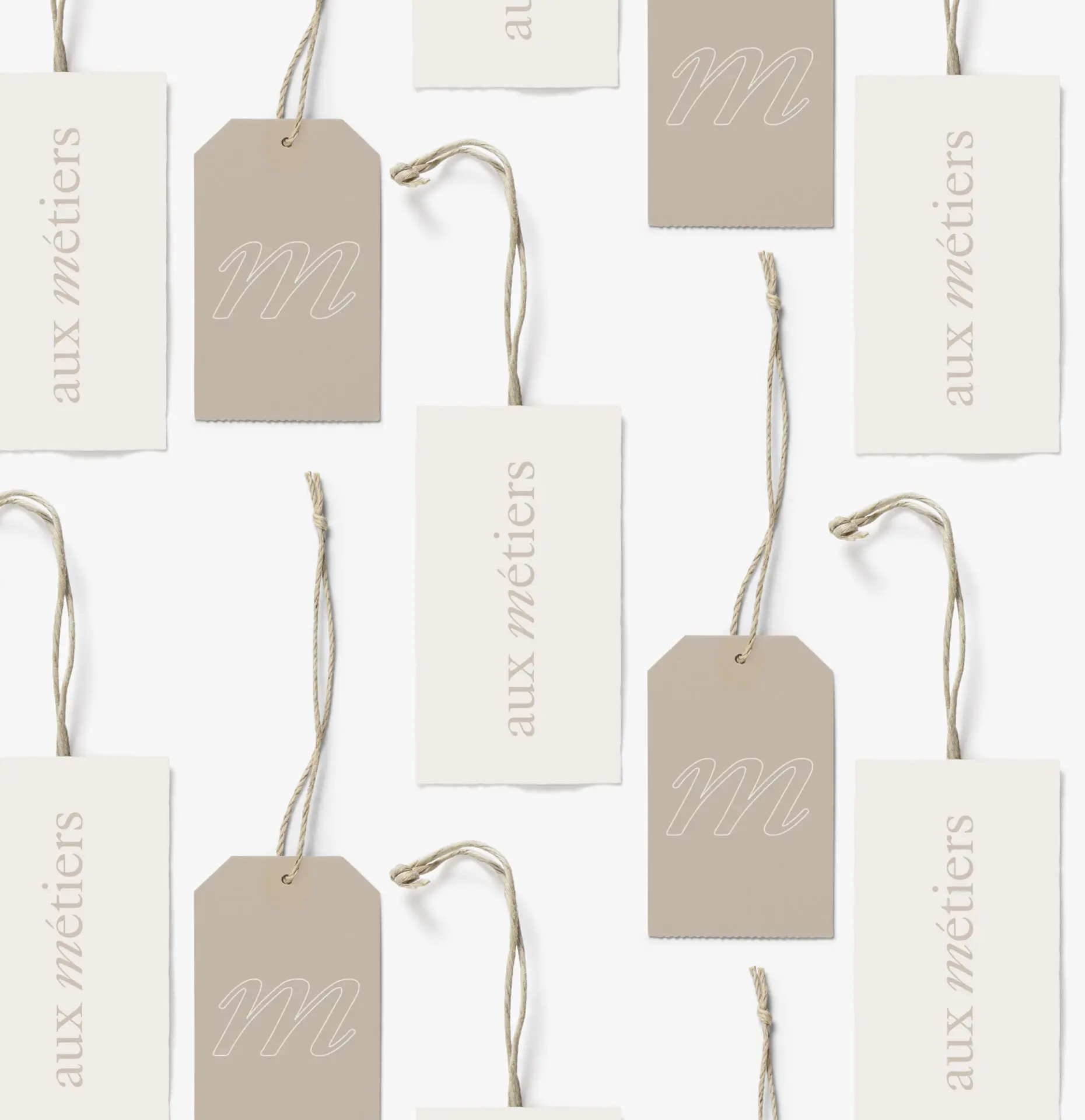 Étiquettes Aux Métiers crème et beige, suspendues à des cordons, avec le logotype et le monogramme m cursif.